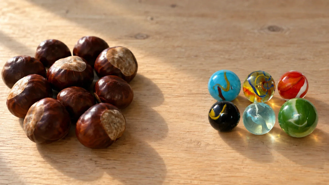 Tas de marrons d'Inde à gauche, six billes de verre MesBilles rangées à droite, sur une table de bois clair