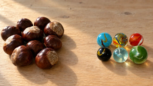Tas de marrons d'Inde à gauche, six billes de verre MesBilles rangées à droite, sur une table de bois clair