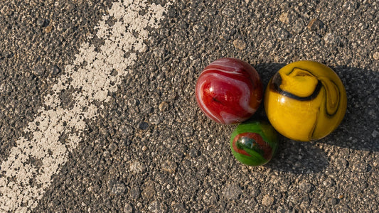 Trois billes de verre MesBilles posées sur le bitume d'une cour, le long d'un tracé de peinture blanche à demi effacé